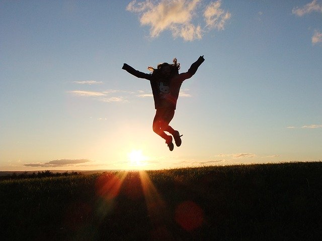 Una noi saltant i al fons el sol surt