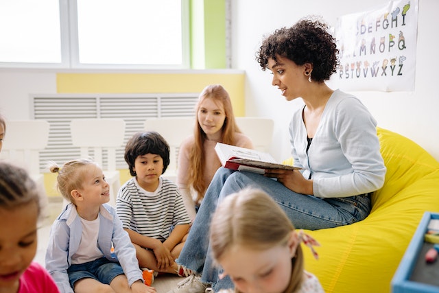 Mestra llegint un llibre a uns nens seguts davant seu
