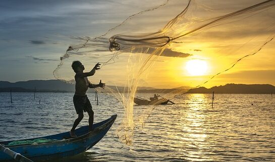 Pescador en una barca llançant una xarxa al mar